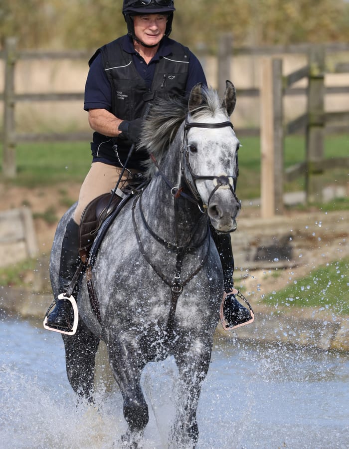 Rider on grey horse splashing through water
